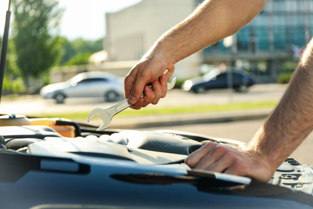 Main tenant une clé à molette sur un moteur de voiture ouvert, effectuant une réparation auto.