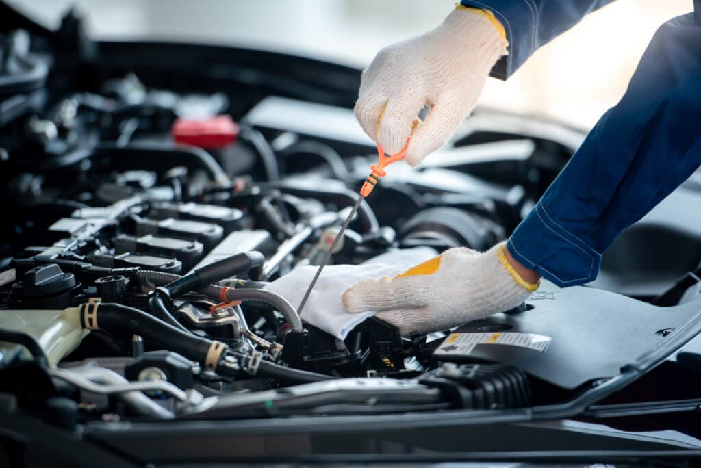 Mécanicien ganté vérifiant le niveau d'huile moteur d'une voiture avec une jauge orange. Gros plan sur les mains et les composants du moteur.